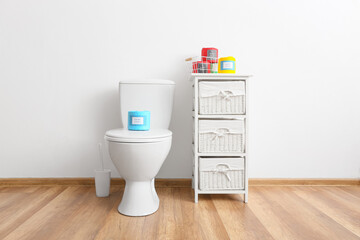 Interior of stylish restroom with toilet bowl and paper rolls on shelf unit