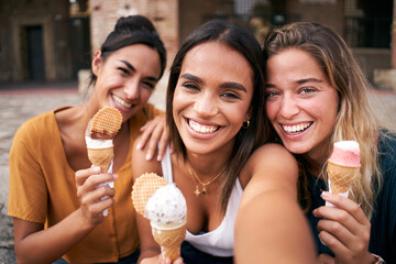 Three young smiling hipster women taking selfie outdoors in summer clothes eating ice cream. Female 20s friends having fun and enjoying summer vibes together. Holiday vacation time