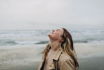 young blonde curly girl smiling and having fun outdoor on a background of hazy sunshine through a thick mist on a calm sea and blue skies