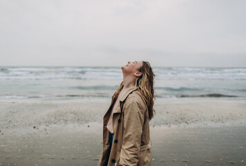 in the photo, a young beautiful blonde curly girl smiles and has fun outdoors against the backdrop of a foggy sun through thick fog on a calm sea and blue sky