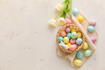Basket with painted Easter eggs, tulip flowers and bunny on light background