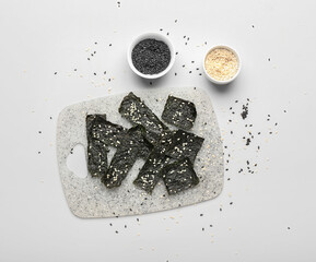 Board with tasty seaweed sheets and bowls of sesame on light background © Pixel-Shot