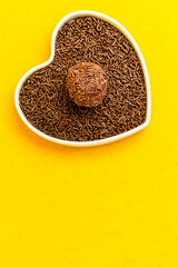 Brigadeiro over a heart-shaped bowl on a yellow background. I love brigadier.