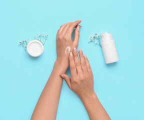 Woman with beautiful manicure applying cream on blue background, closeup