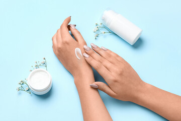 Woman with beautiful manicure applying cream on blue background, closeup