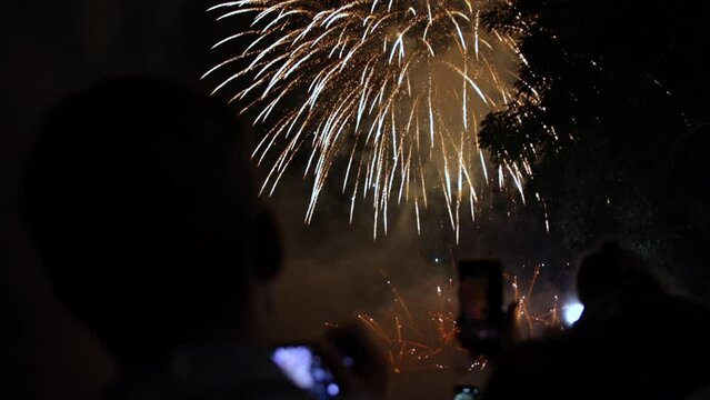Shoots fireworks video on smartphone, hand of man taking the photo of fireworks by smartphone. Shoots fireworks on a smartphone. The lights are beautifully reflected in phone screen.