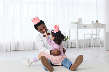 Happy African-American man and his little daughter in paper crowns playing at home