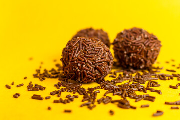 Three Brazilian Brigadeiros with sprinkles scattered on a yellow background with copy space.