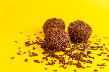 Three Brazilian Brigadeiros with sprinkles scattered on a yellow background with copy space.