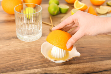 Woman squeezing orange for juice on wooden table, closeup