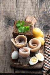 Homemade marinated herring roll with rye bread and baby potato with quial eggs on wooden table