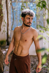 Portrait of an attractive shirtless Spanish man with a beard and hair highlights posing in a garden