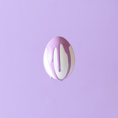 Obraz premium A white Easter egg on a pastel purple background from which purple paint is dripping. Easter egg aesthetic monochrome concept.