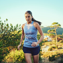 Keeping a steady but strong pace. Shot of a young woman out for a run along a mountain trail.
