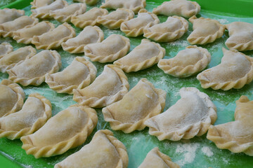 Uncooked dumplings on a green kitchen tray with flour