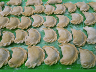 Semi-finished dumplings on a green kitchen tray with flour