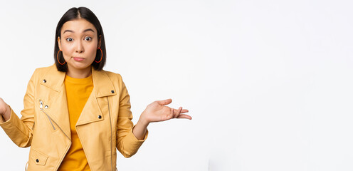 Image of korean girl shrugs shoulders and looks confused, dont know, cant tell, standing over puzzled over white background
