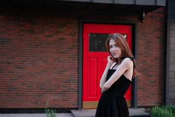 charming young woman in a black dress in front of modern building with red door. housewarming. buying a house. happy life in private house