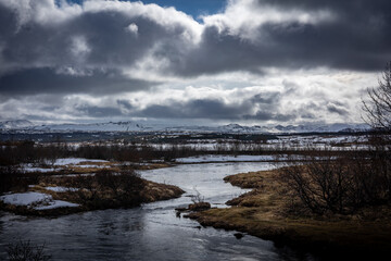 A lake in suburbs of Reykjavik, Iceland. Snowy mountain range in background, cloudy sky. 