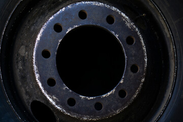 Close up of an old black damaged steel rim from a bus or a truck. Scratched rusted metal part of a wheel