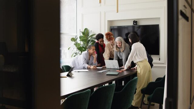 Slow motion view through open doorway towards group of businesswomen discussing with laptop on meeting room table