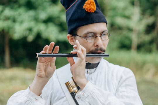 A male soldier in a white uniform plays the flute.