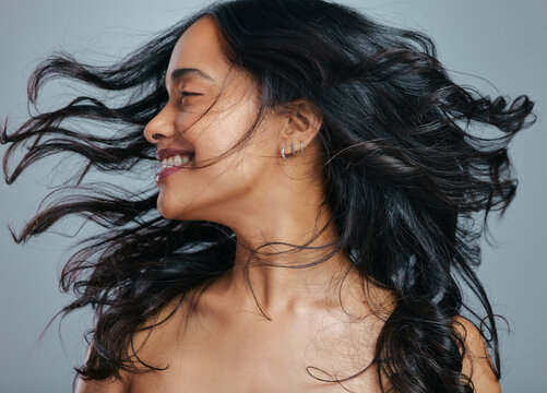 Her Hair Has Natural Bounce And Great Volume. Studio Shot Of An Attractive Young Woman Tossing Her Hair Against A Grey Background.