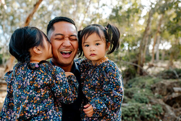 Asian dad holding daughters outdoors
