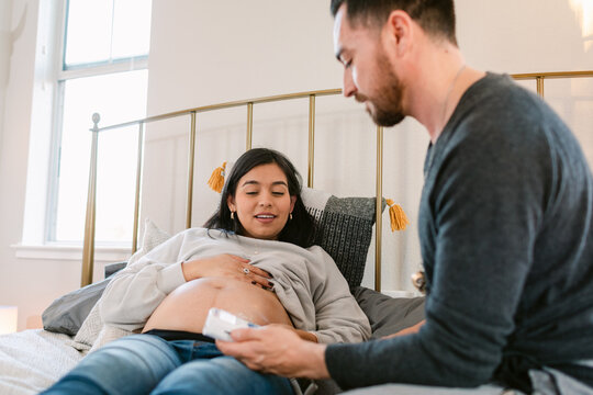 Couple In Bedroom Using Fetal Monitor 