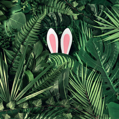 Creative Easter nature background. Green tropical palm leaves with pink Easter bunny ears. Minimal...