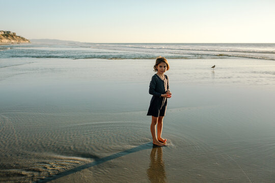 Girl standing in water on beach at sunset