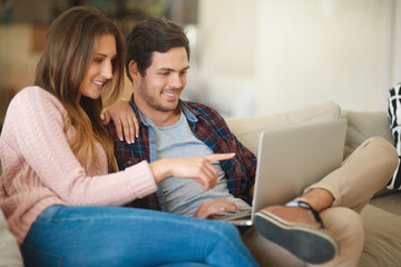 House hunting from the comfort of their couch. Shot of a happy young couple using a laptop together...