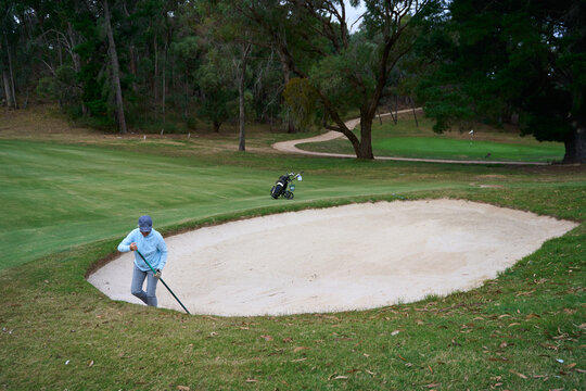 A golfer rakes sand bunker