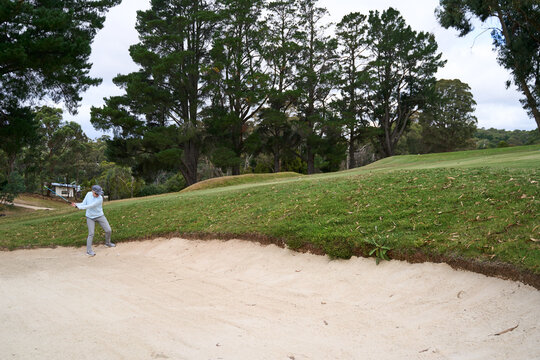 A female golfer hitting out of a sand bunker