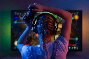 A gamer or a streamer girl at home in a dark room with a gamepad playing with friends on the networks in video games. A young man sits in front of a monitor or TV. © Anton