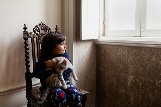 Girl holding cat looking by the window at home