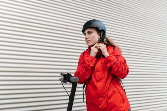 Woman in uniform fastening helmet before riding e scooter