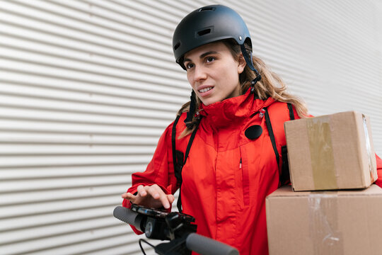 Female courier on scooter with boxes using smartphone