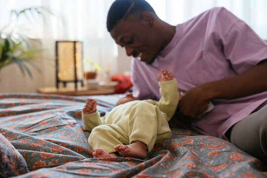 Black father relaxing with baby on bed