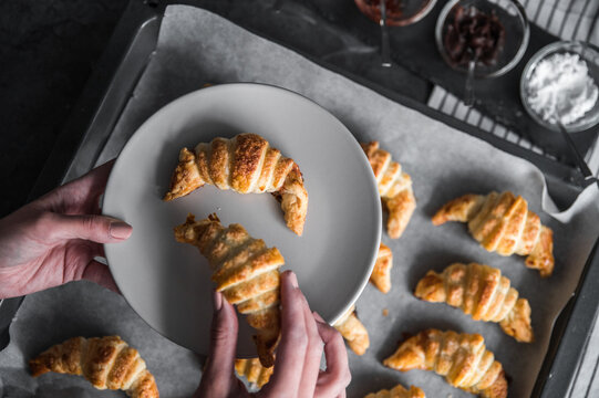 Crop woman putting croissants on plate