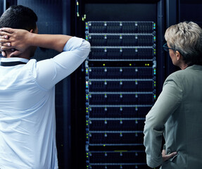 Anybody know a good IT guru. Rearview shot of two technicians looking stressed while working in a data centre.