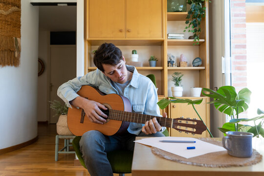 Young man playing guitar at home and writing a song