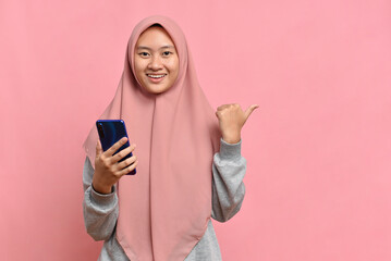 Asian Muslim woman holding a phone and pointing at copy space