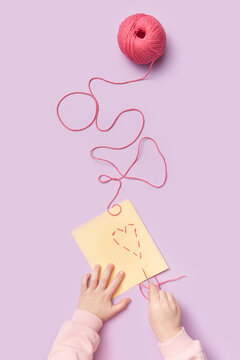 Little kid sewing heart on yellow paper