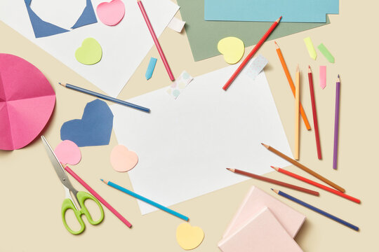 Beige background with pencils, paper sheets and scissors