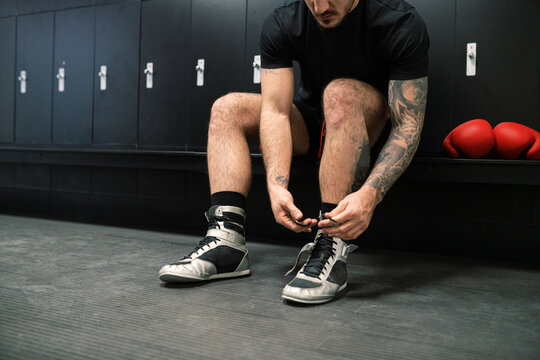 Anonymous male boxer tying boots in locker room before training