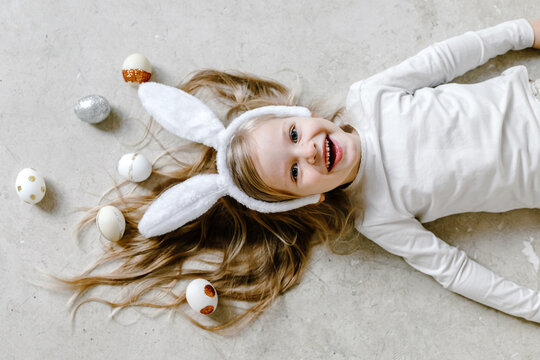 Funny kid in bunny ears on floor with Easter eggs