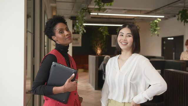 Slow Motion Of Mature Black Woman With Tablet, And Mid Adult Chinese Woman, Smiling And Looking At Camera In Co Working Office Space