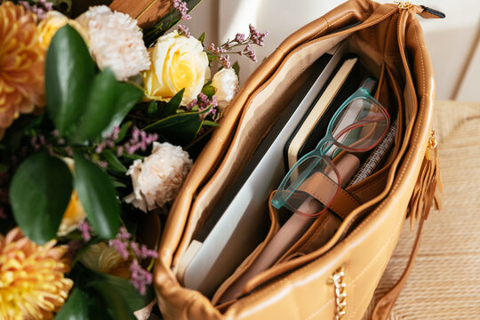 Handbag with eyeglasses and laptop near flower bouquet