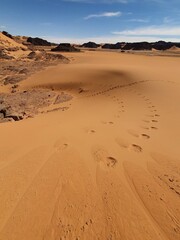 Fototapeta na wymiar Parallel footprints in a turn path crest of an orange colored sand dune. High angle view with rock stones below. Tassili N'Ajjer, Tadrart Rouge, Djanet. Algeria.